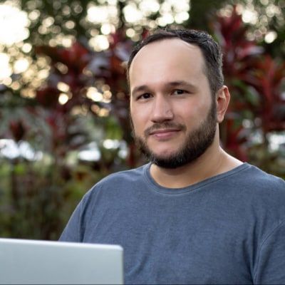 Gilberto Tavares smiling outdoors, with a laptop in front of him